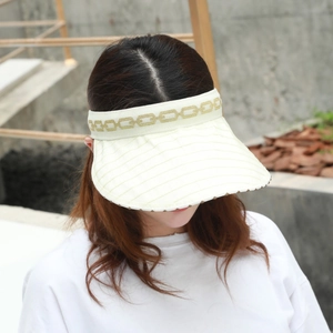Detail of cream sun visor hat with gold chain pattern and breathable woven fabric texture