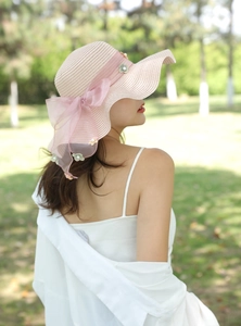 Dettaglio cappello di paglia rosa a tesa larga con fiocco in tulle e fiori di perla