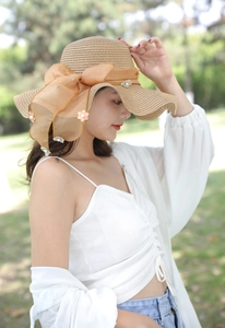 Dettaglio cappello di paglia con fiocco arancione e fiori decorati con perle