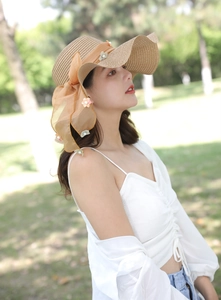 Dettaglio cappello di paglia a tesa larga con nastro di chiffon arancione e fiori
