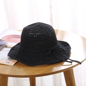 Detail of black crochet sun hat with bow decoration on wooden table with accessories