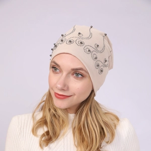 Detail of beige knit beanie featuring elegant grey beads and metal rivet floral patterns