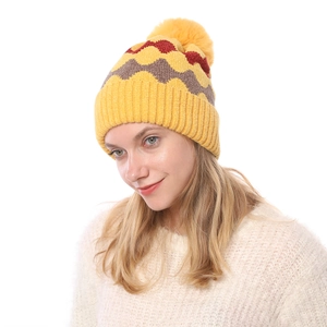 Detail der Strickstruktur einer Wintermütze mit gelben Wellenmustern und Kunstpelz-Bommel