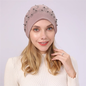 Detail of dusty pink cotton beanie with wavy silver beaded patterns on a model