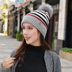 Detail der Strickstruktur einer grauen Streifenmütze mit Kunstfellpompon und M-Metalllogo