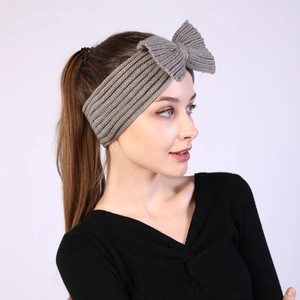 Close-up of a grey knitted headband with a large bow detail worn by a fashion model