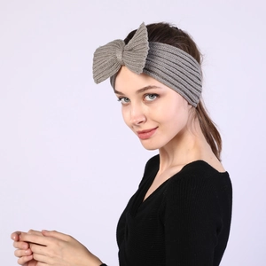 Detailed side view of a grey knitted bow headband worn by a model for winter warmth
