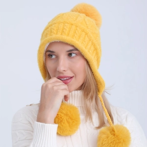 Dettaglio del cappello in maglia gialla con fodera in peluche e tre pompon decorativi