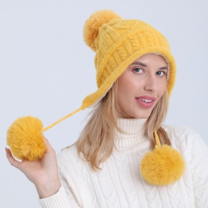 Dettaglio del cappello in ciniglia gialla con tre grandi pompon in pelliccia sintetica e paraorecchie