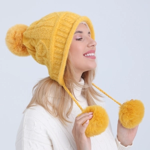 Dettaglio del cappello in maglia gialla con paraorecchie e morbidi pompon in ciniglia