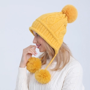 Dettaglio cappello giallo in maglia a trecce con paraorecchie e tre morbidi pompon