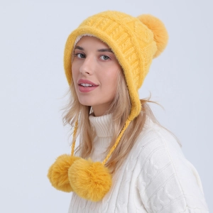 Dettaglio del berretto in maglia gialla con fodera in peluche e tre pompon