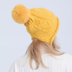 Dettaglio del berretto giallo in maglia a trecce con grande pompon e paraorecchie