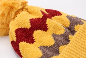 Detail der gelben Strickmütze mit geometrischem Muster und flauschigem Bommel-Akzent