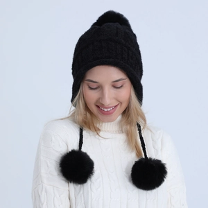 Dettaglio del cappello in maglia nera con tre pompon di pelliccia su modella invernale