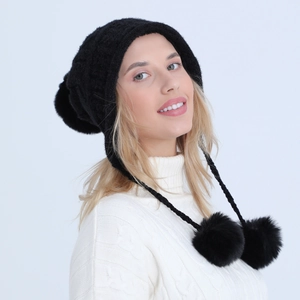 Dettaglio del cappello in maglia nera con paraorecchie e grandi pompon in finta pelliccia