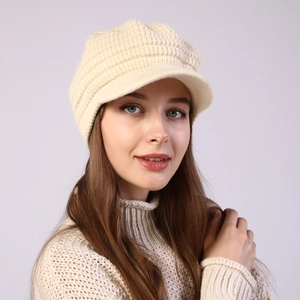 Close-up of creamy white knitted newsboy hat with thick striped texture and visor