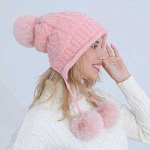 Dettaglio cappello in ciniglia rosa lavorata a maglia con paraorecchie e grandi pompon