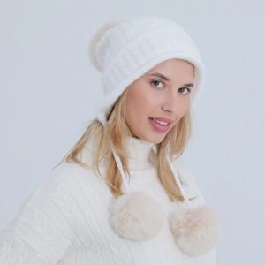 Dettaglio del cappello in maglia di ciniglia bianca con morbidi pompon e paraorecchie