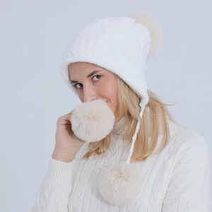 Dettaglio del berretto in maglia bianca con paraorecchie e tre grandi pompon beige