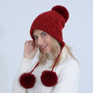 Dettaglio del cappello invernale rosso a maglia trecciata con ciniglia e tre pompon di pelliccia