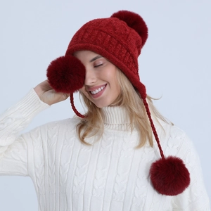 Dettaglio del berretto in maglia rosso scuro con pompon in ecopelliccia e paraorecchie