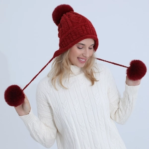 Dettaglio cappello a trecce rosso con grandi pompon in finta pelliccia sui paraorecchi
