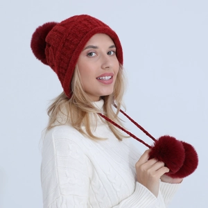 Dettaglio di cappello in maglia rosso scuro con pompon di peluche e lacci intrecciati