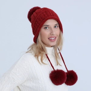 Dettaglio del cappello rosso in maglia a trecce con tre pompon e cordoncini auricolari