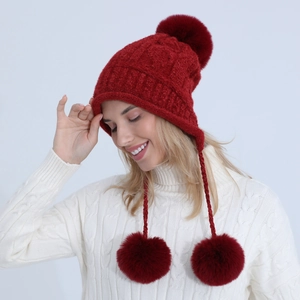 Dettaglio del cappello rosso in maglia a trecce con pompon e paraorecchie per più calore