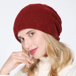 Close-up of a deep red knitted beanie with diamond pattern on a model in white sweater