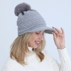Detail of grey knitted winter hat featuring a soft pom-pom and a stylish peak brim