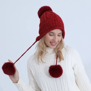 Dettaglio del cappello rosso in maglia di ciniglia con paraorecchie e tre pompon morbidi