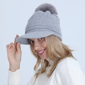 Detailed knit texture of grey peak cap with fluffy faux fur pompom and soft lining