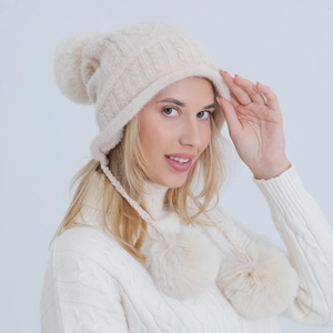 Dettaglio del berretto in maglia bianco crema con morbidi pompon e paraorecchie invernali