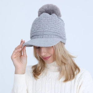 Detail of light gray knit beanie with visor and soft faux fur pompom for winter wear