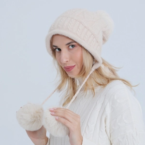 Dettaglio del cappello in maglia crema con pompon morbidi e trame a treccia calde