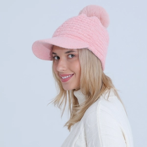 Close-up of light pink cable knit beanie with brim and large faux fur pom-pom detail
