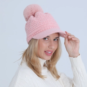 Detail of pink knitted winter hat with visor and fluffy faux fur pom-pom on top