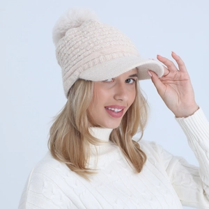 Detail view of winter knit beanie with brim and large beige pompom featuring cable texture