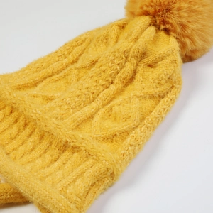 Dettaglio della cuffia gialla a maglia intrecciata con un pompon soffice in ecopelliccia