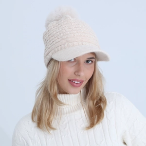 Detail view of the beige knit beanie with a fluffy faux fur pompom and curved brim
