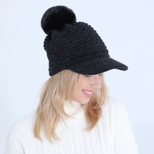 Close-up of black cable knit hat with brim and fluffy faux fur pompom for winter