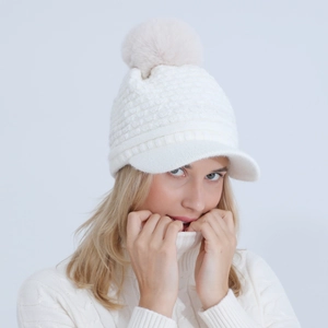 Detail of white cable knit beanie with faux fur pompom and soft peak visor for women