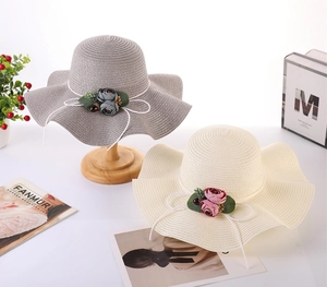 Detail of wide brim straw hats in grey and beige featuring floral and bow accents