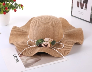 Detail of wide brim straw sun hat with pink floral accents and wavy edge design
