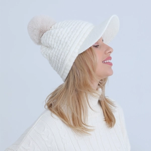 Detail view of white knit winter hat with fuzzy pompom and visor on a female model