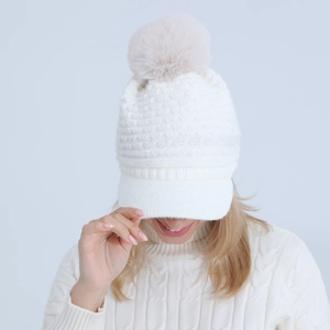 Detail of cream knit beanie with fluffy faux fur pompom and stylish visor for winter