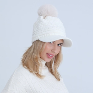 Close-up of white knit beanie with soft brim and plush faux fur pompom for winter warmth