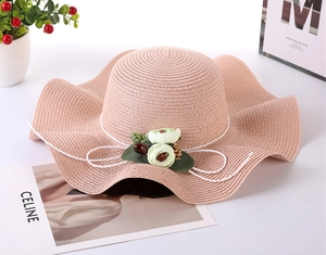 Close-up of pink straw sun hat with wavy brim, flower decor and white rope knot